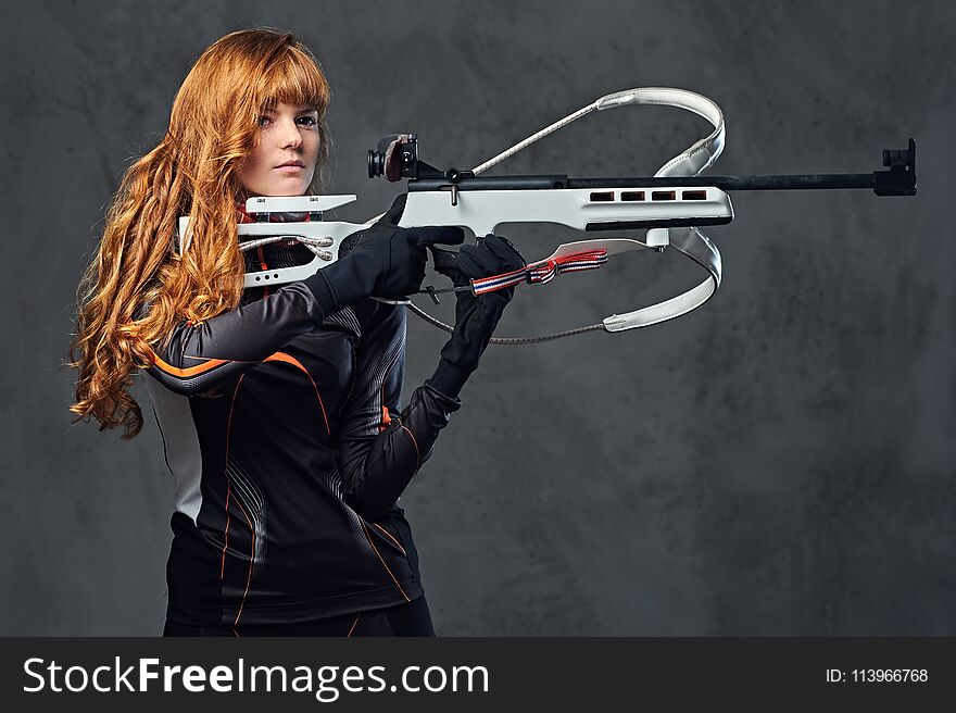 Redhead female Biathlon champion aiming with a competitive gun.