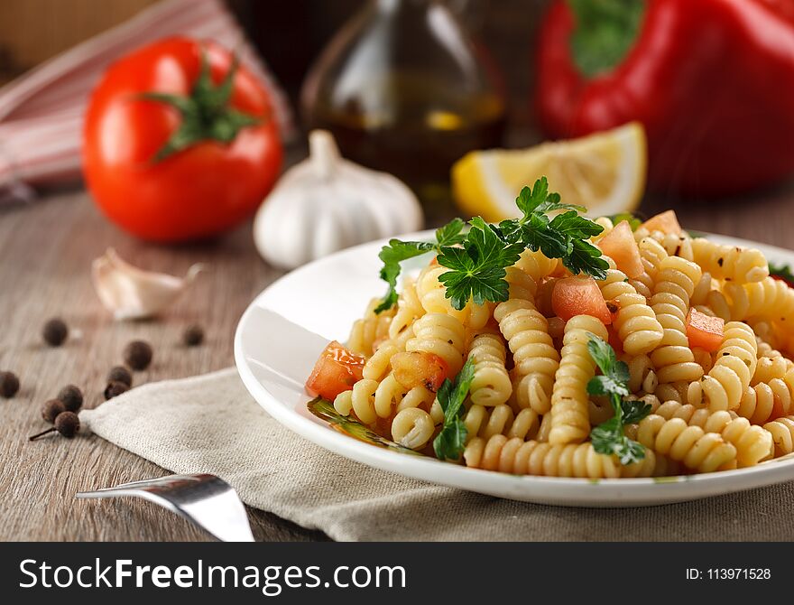 Vegetarian vegetable pasta Fusilli with tomato, parsley and olive oil in white plate on wooden table. Vegetarian vegetable pasta Fusilli with tomato, parsley and olive oil in white plate on wooden table.