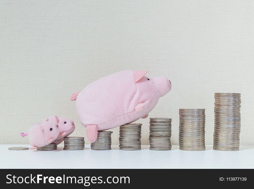 Closeup pile of coin start from low to high with pig doll and three little pig walk to the top of coin on wood desk and wallpaper textured background in success of saving money concept