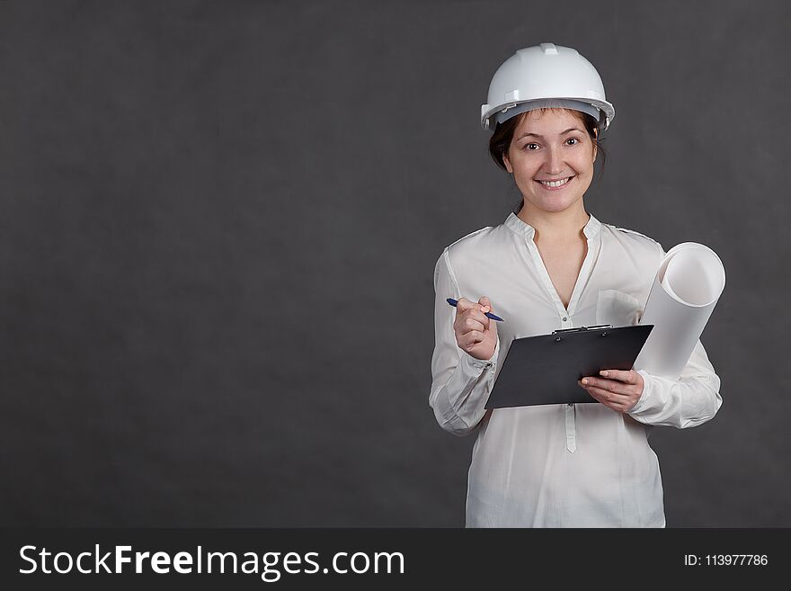 Young female architect in a protective helmet makes notes on the project with a paper in hands.
