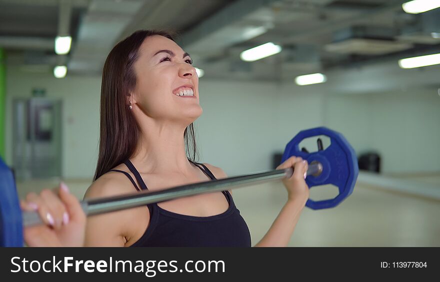 Fitness concept. Beautiful brunette woman doing exercises at the arm with a barbell.