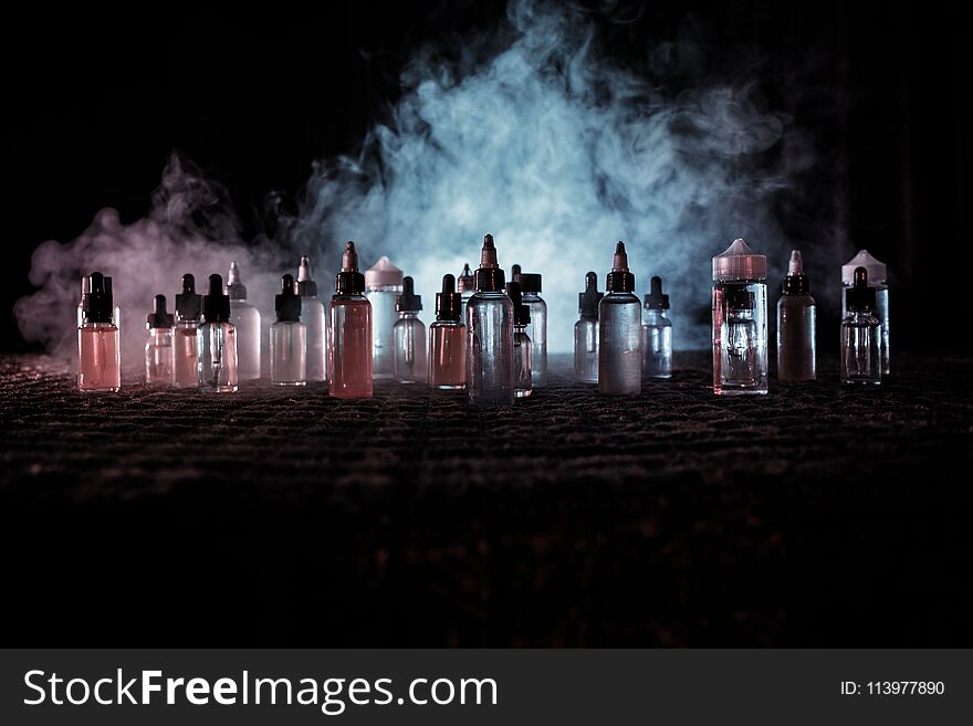 Vape Concept. Smoke Clouds And Vape Liquid Bottles On Dark Background. Light Effects. Useful As Background Or Vape Advertisement O