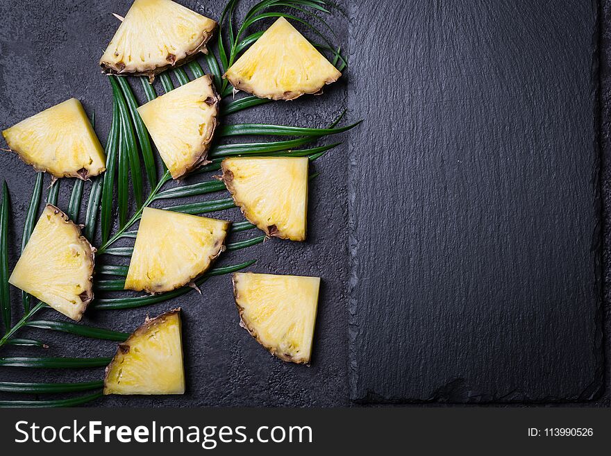 Sliced pineapple and palm branch on a black background.