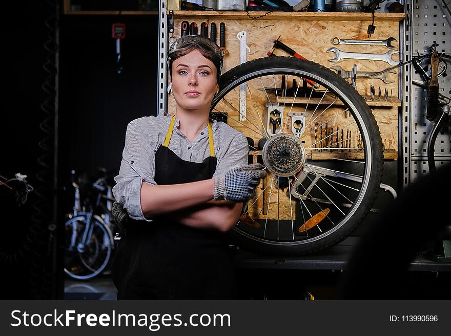 Portrait of a beautiful brunette female wearing working clothes, apron and goggles, standing in a workshop.