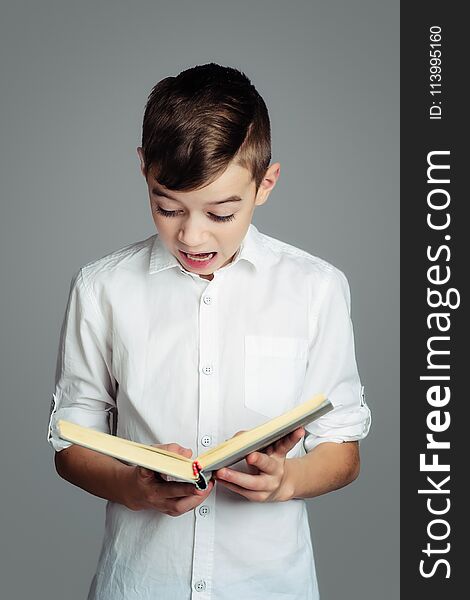 The boy is reading a book, an expression of surprise and fear on his face