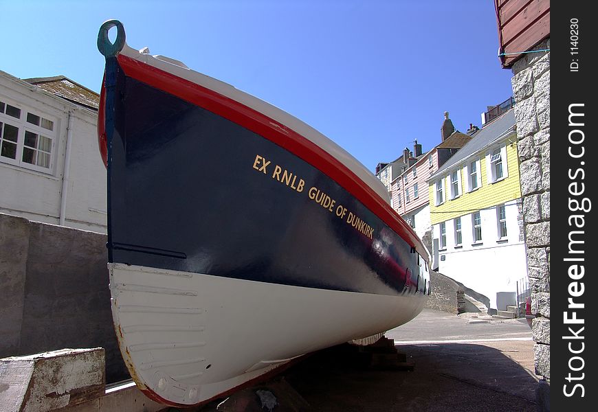 Old lifeboat at Mevagissey harbor in Cornwall with colorful houses in background