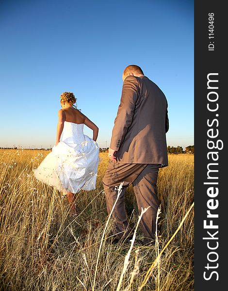 Bride and groom walking in field of grass. Bride and groom walking in field of grass