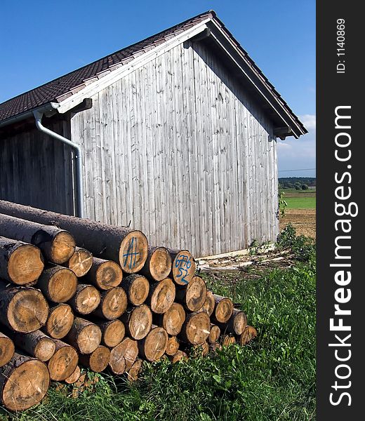 The image shows a grey, weathered hut made of wood with a pile of logs in front of it. The picture was taken in Bavaria (Germany). In the background of the photo is deep blue sky. The image shows a grey, weathered hut made of wood with a pile of logs in front of it. The picture was taken in Bavaria (Germany). In the background of the photo is deep blue sky.