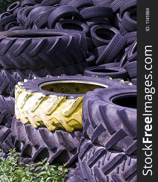 The picture shows a pile of old tires. In the back of the image there are small tires, like for normal cars. In the front of the photo there are some big traktor tires. One of them is painted with yellow color. The picture shows a pile of old tires. In the back of the image there are small tires, like for normal cars. In the front of the photo there are some big traktor tires. One of them is painted with yellow color.