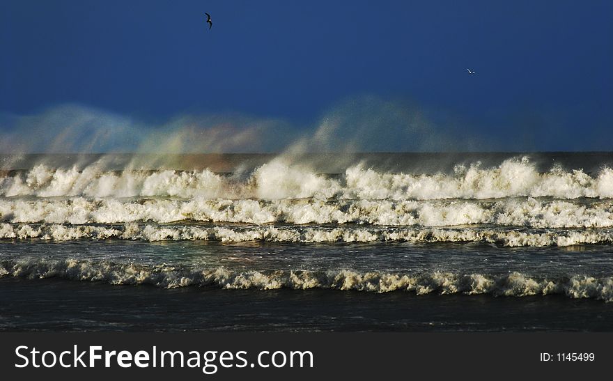 Waves breaking on the beach with rainbow colours in the spray. Waves breaking on the beach with rainbow colours in the spray