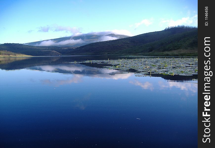 A dam early in the morning with the reflection of the mountains and the clouds in the water. A dam early in the morning with the reflection of the mountains and the clouds in the water