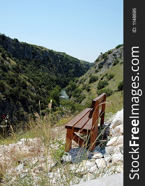 A wooden bench on the top of a hill and a river in the background. A wooden bench on the top of a hill and a river in the background