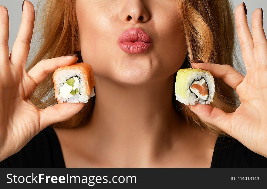 Closeup woman with sushi hold philadelphia rolls in hands show kissing sign on a light gray background