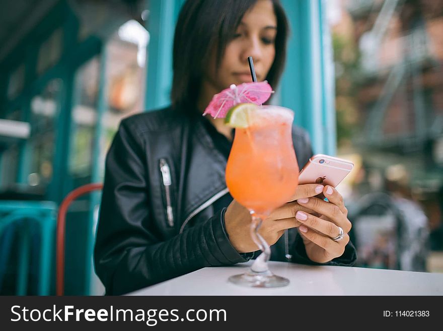 Woman Holding Mobile Phone With A Cocktail Glass On The Table