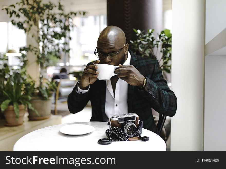 Man Sitting in Front of Round Table While Sipping from White Ceramic Mug