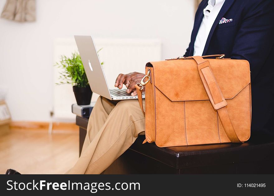 Person Wearing Blue Suit Beside Crossbody Bag and Using Macbook