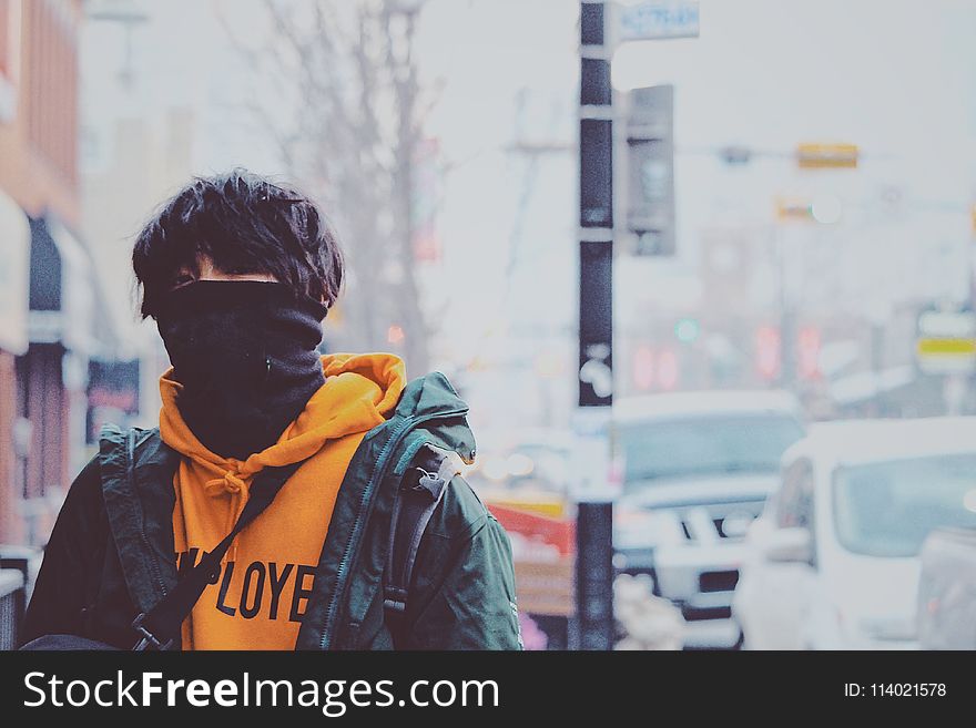 Man in Orange Pullover Hoodie and Green Jacket Covered With Black Mask