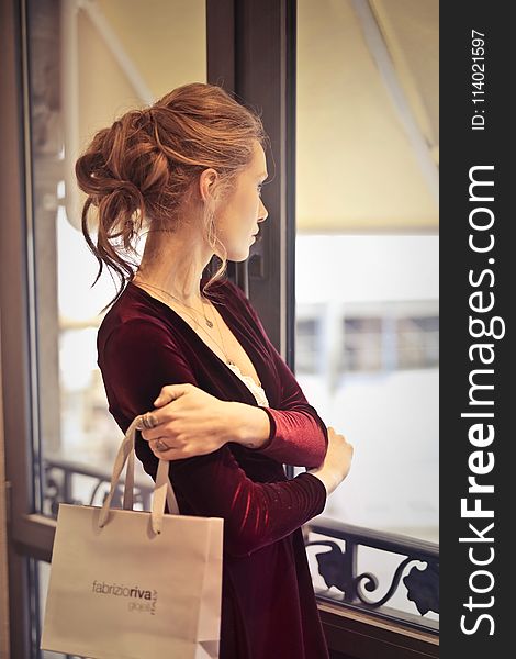 Woman Holding White Paper Bag While Looking at the Window