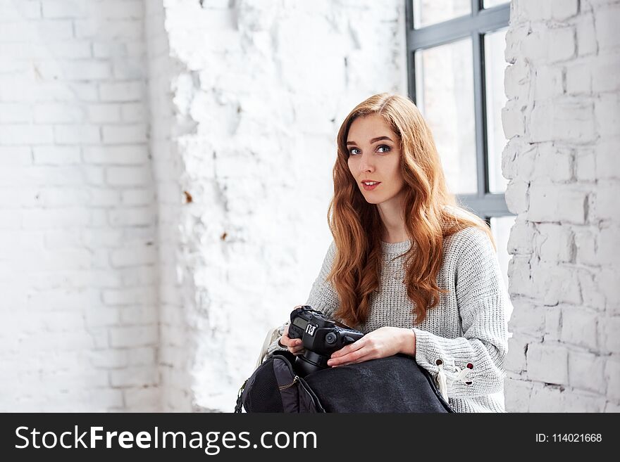 Young female photographer with camera sitting near window in photo studio
