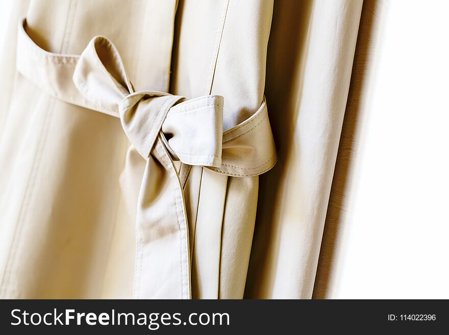 A greige or beige elegant trench coat with ribbon over white.Close up