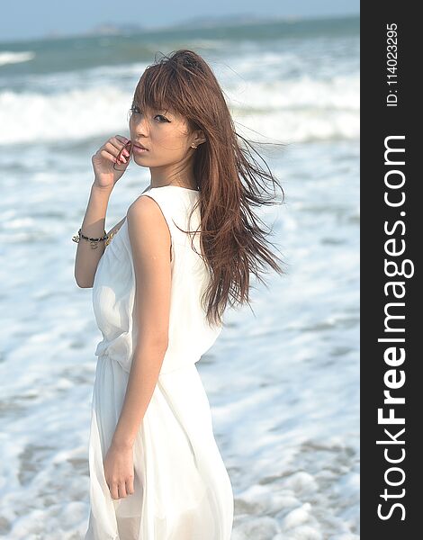 Beautiful asian girl playing on the beach, a white dress, sweet smile, the sea breeze blowing hair