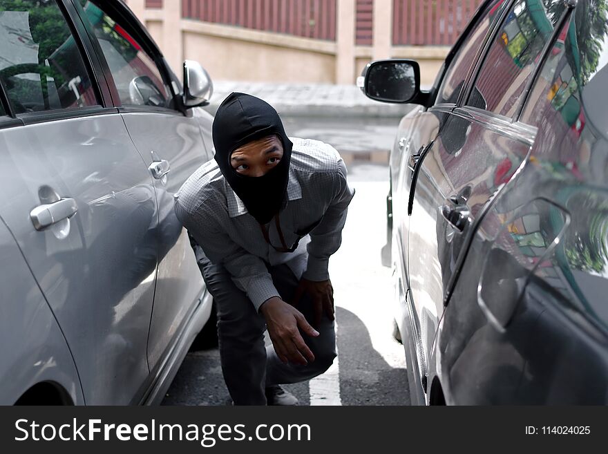 Thief in black balaclava trying to break into car