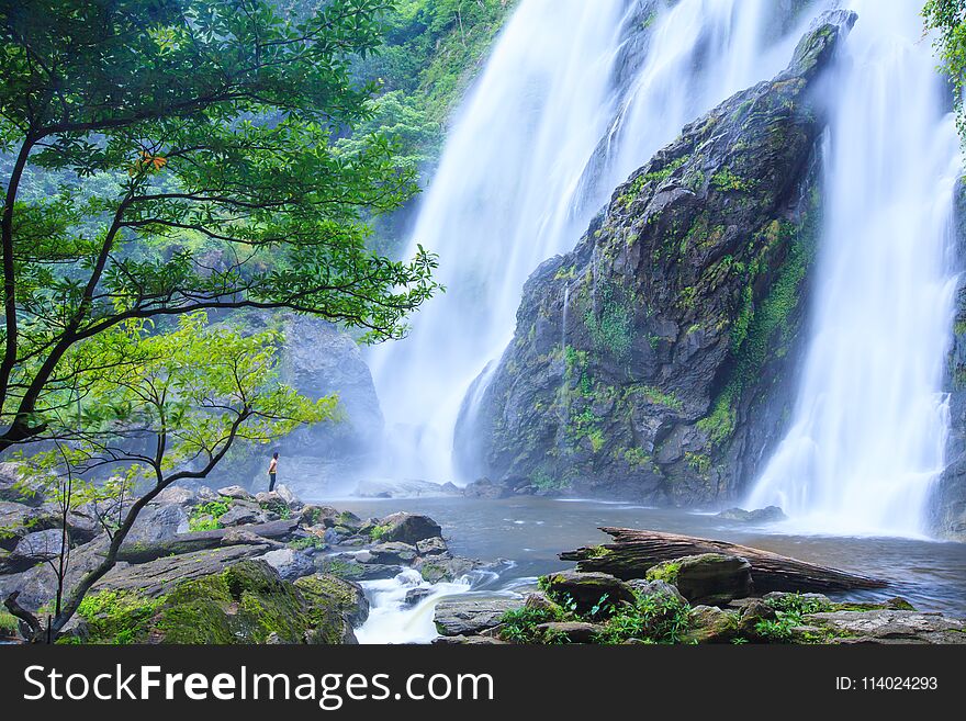 Young Man Relaxing On Stone In Front Of Flowing Waterfall. Nature Therapy.