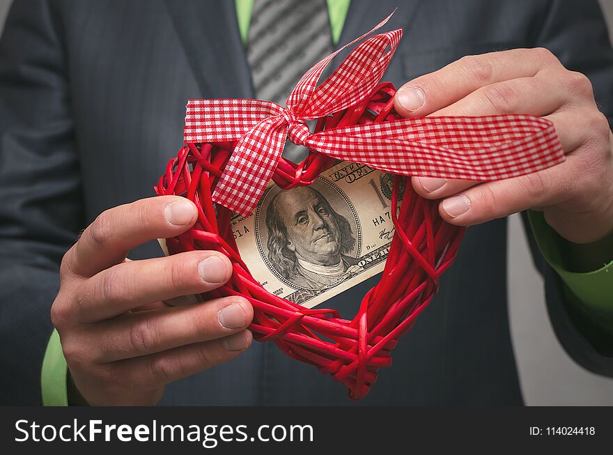 Red heart shape and one hundred dollars in businessman hands. Love for money. Greedy man. Miser.