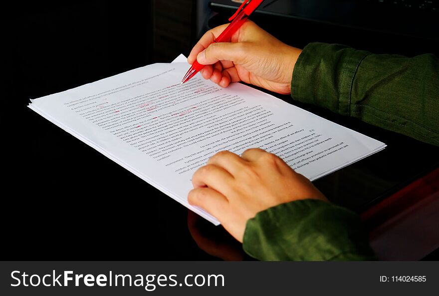 Hand holding red pen to correct proofreading paper on black table in office. Hand holding red pen to correct proofreading paper on black table in office
