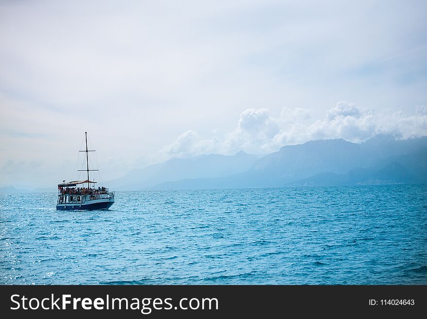 The ship sails on the sea. A boat with tourists sails along the coast. A sea ship alone in the background of a beautiful sky.