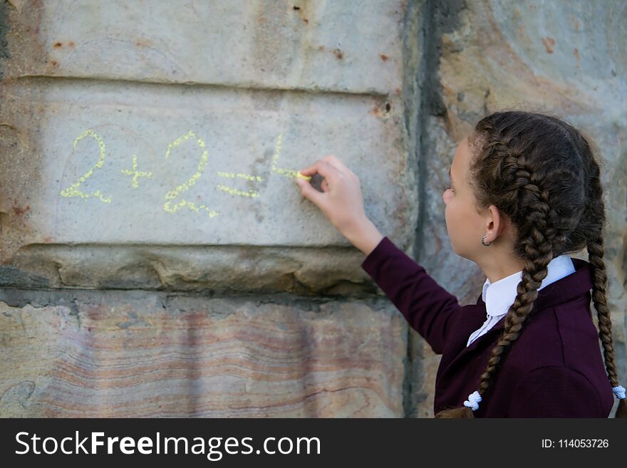 Girl with pigtails, wrote a mathematical example on a stone wall. schoolgirl