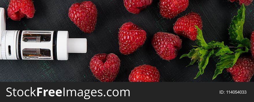 White electronic cigarette, on a black painted board, next to a green mint, and a red raspberry