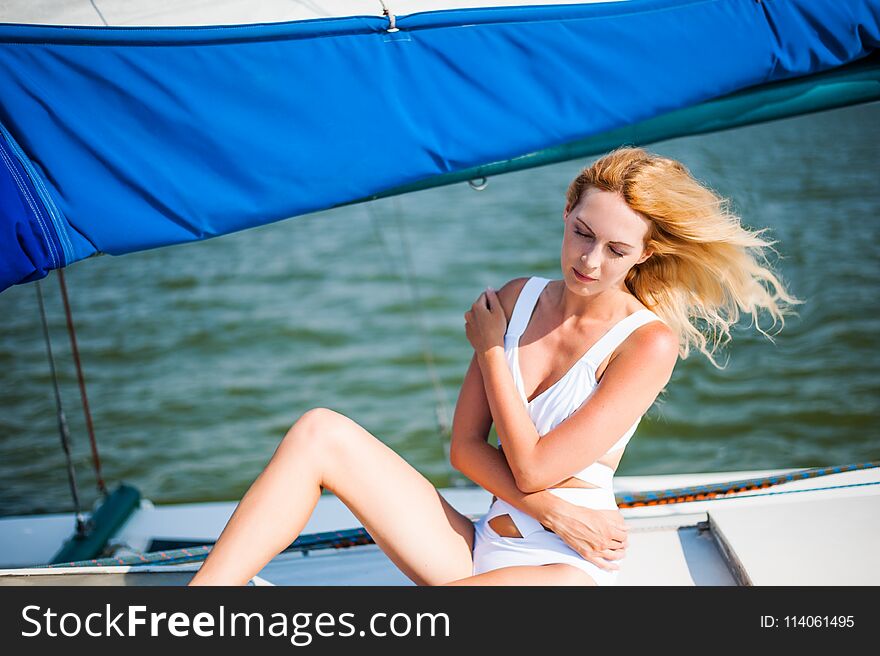 Portrait of beautiful young fashion woman sitting on sail boat or yacht in the sea wearing modern swimsuit