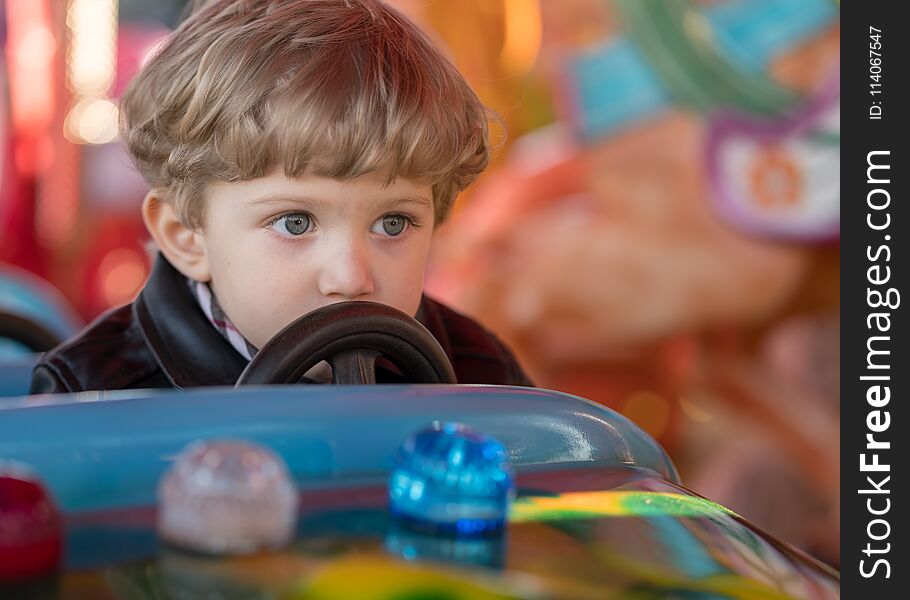 Kid boy drives a blue car at carousel