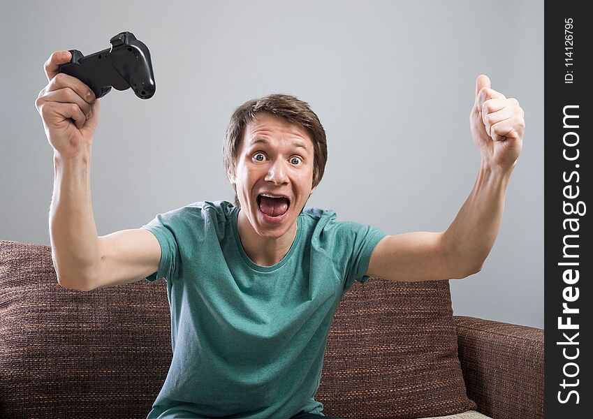 Handsome young man with smile sitting on sofa and holding controller and playing video games. Cheerful dude on sofa having fun with internet friends. Handsome young man with smile sitting on sofa and holding controller and playing video games. Cheerful dude on sofa having fun with internet friends