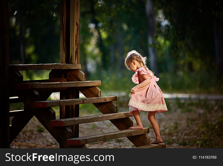 Beautiful little girl with funny face expressions playing, climbing up on a wooden stairs