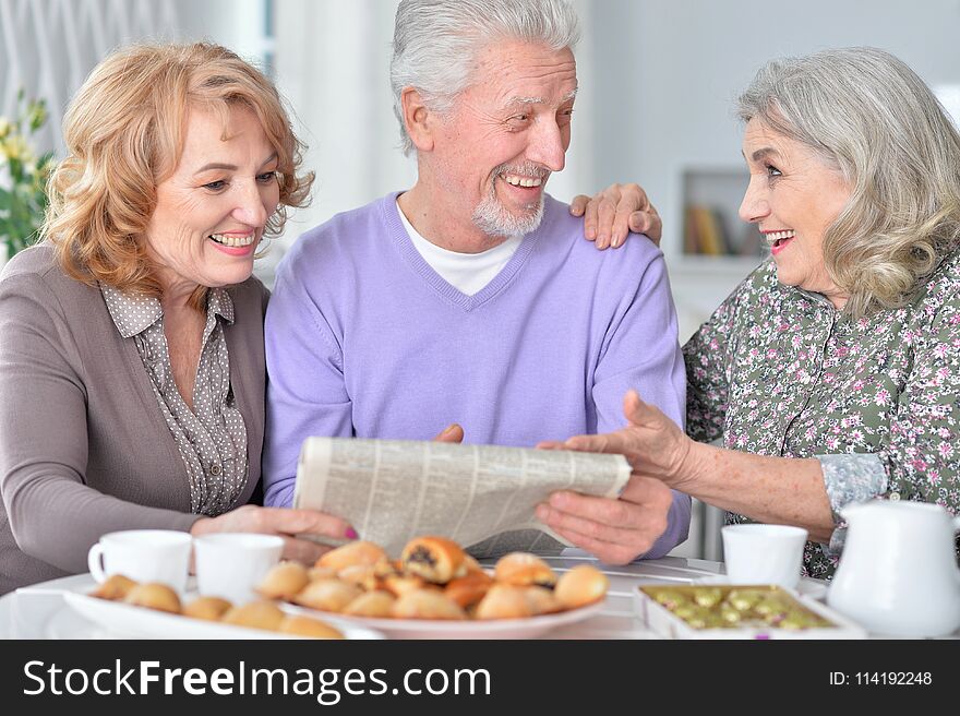 Portrait of happy senior people drinking tea and reading newspaper