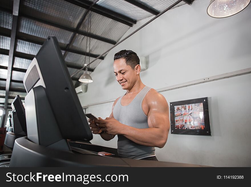 Muscular man on treadmill holding smartphone in the gym centre