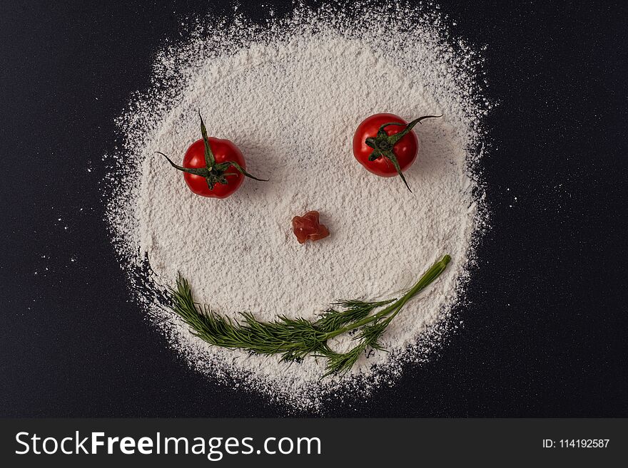 Photo of smiling faces from tomato parsley flour lying on a black. Concept