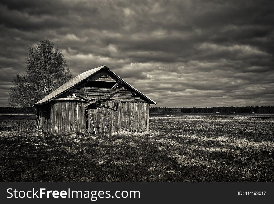 The late spring comes with the heavy clouds on the old barn house in the rural Finland. The tree is bare and nothing much is growing on the fields. The late spring comes with the heavy clouds on the old barn house in the rural Finland. The tree is bare and nothing much is growing on the fields.