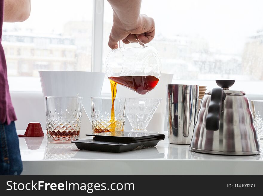 A man pours coffee for a sample from a decanter into faceted transparent glasses. A man pours coffee for a sample from a decanter into faceted transparent glasses.