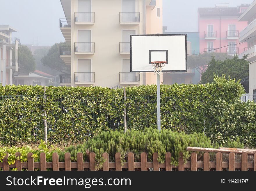 Basketball structure in an outdoor playground surrounded by trees in a park.