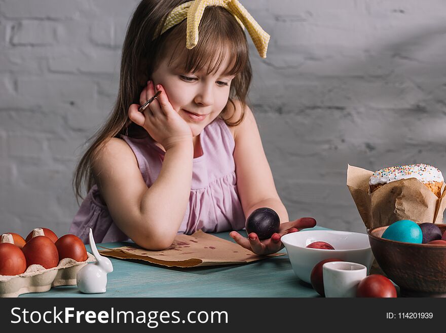 Adorable kid looking at painted egg in hand, easter concept