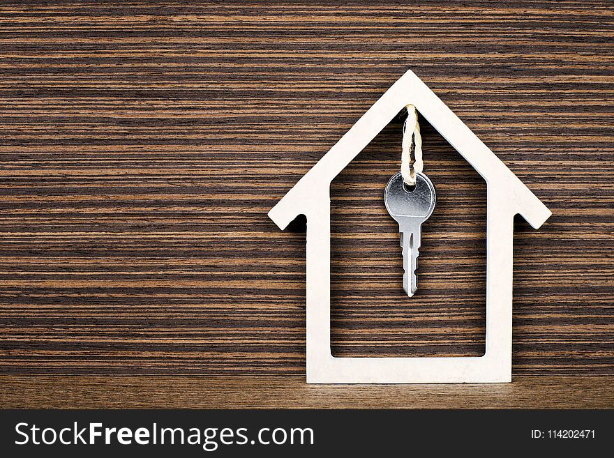 Silver key hanging inside white house on vintage wooden background. Concept for real estate, moving home or renting property. Silver key hanging inside white house on vintage wooden background. Concept for real estate, moving home or renting property.