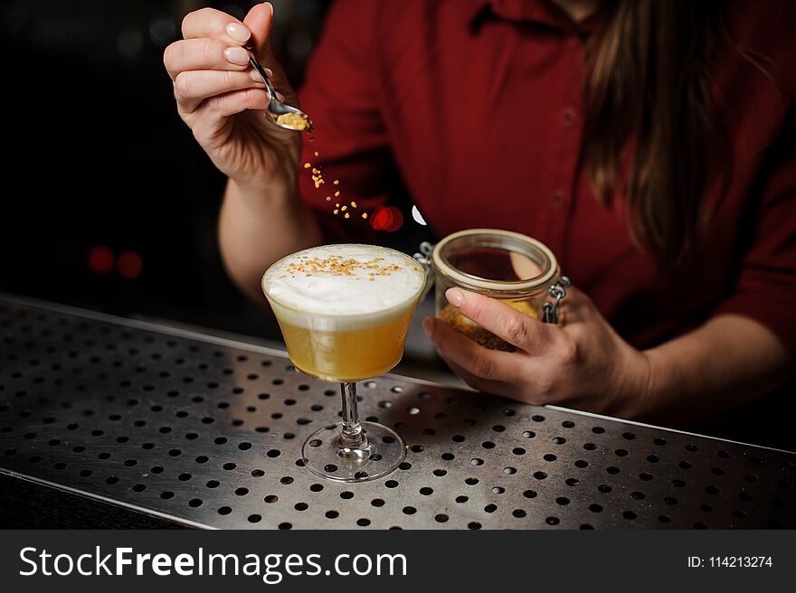 Female bartender serving a fresh delicious yellow cocktail and adding spice to it on the bar counter. Female bartender serving a fresh delicious yellow cocktail and adding spice to it on the bar counter