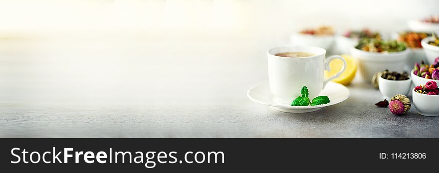 Tea concept with copy space. Different kinds of dry tea in white ceramic bowls and cup of aromatic tea on grey background. Banner.