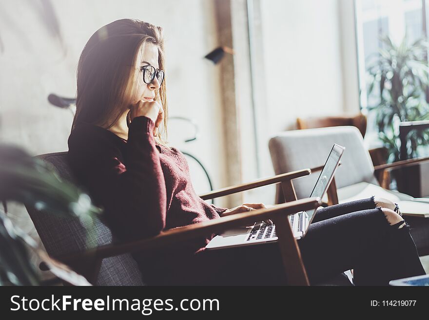 Attractive young businesswoman wearing casual clothes and working at coworking office.Female using contemporary mobile laptop while sitting in comfort armchair