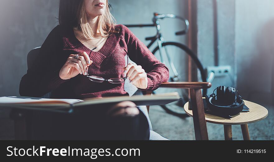 Handsome young girl wearing glasses casual clothes holding book hands.Woman blonde sitting in vintage armchair modern loft studio reading book. Blurred background.Horizontal