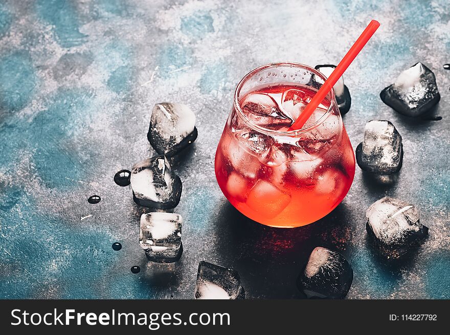 Red cocktail with ice on a black blue surface. Bright, red drink in backlight. Copy space.