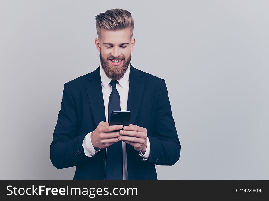 Portrait of handsome with stylish hairdo cheerful funny excited financier using smartphone playing online games receiving getting writing sms updating his digital gadget isolated on gray background. Handsome guy.